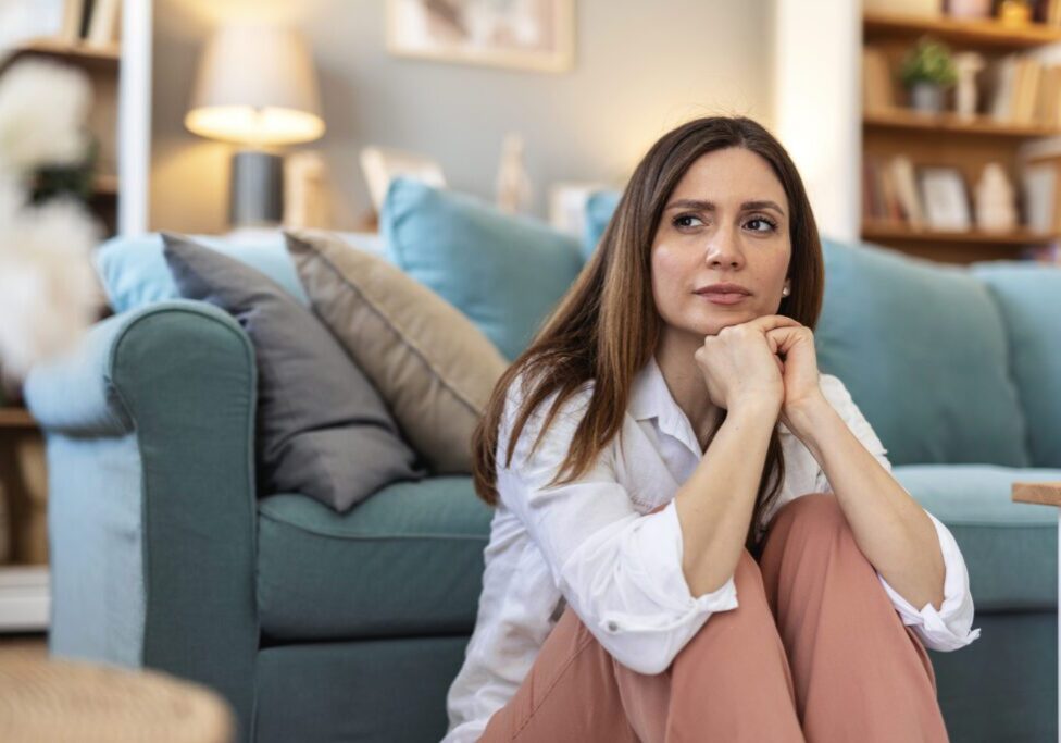 Thinking, sad and woman in home on the floor with anxiety for issue, depression and reflection in living room. Apartment, morning and thoughtful person with worry, overthinking and wondering in house.